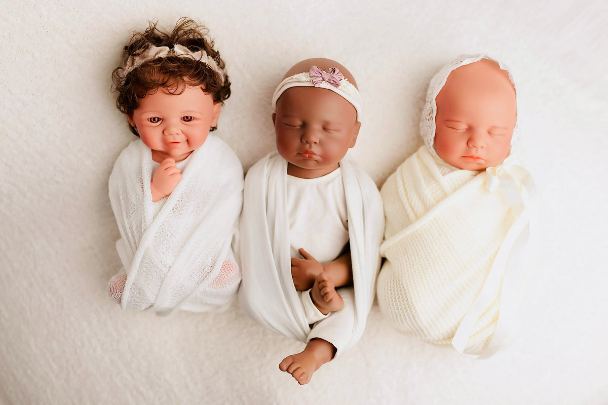 Three swaddled silicone baby dolls with different hair and skin tones side by side