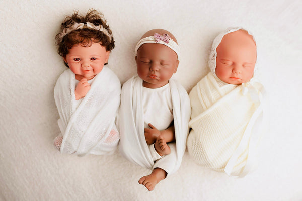 Three swaddled silicone baby dolls with different hair and skin tones side by side