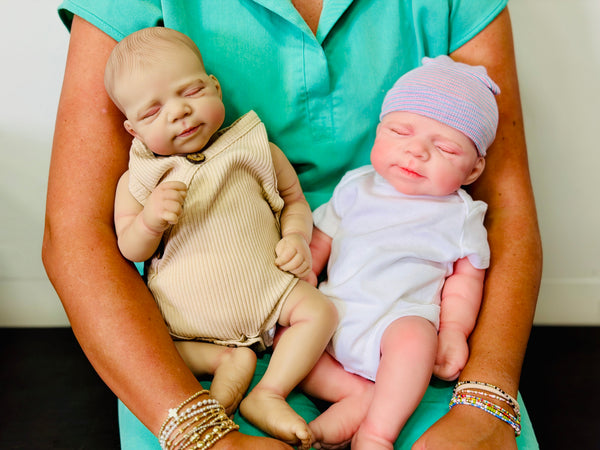 Side-by-side comparison of a vinyl reborn doll and a silicone baby doll being held