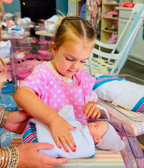 Little girl looking at her silicone baby swaddled in a bassinet during the adoption experience at Little Mamas Nursery